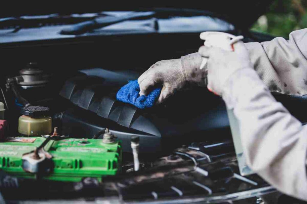 Car engine bay being cleaned with brush and degreaser, showing step-by-step engine cleaning process.