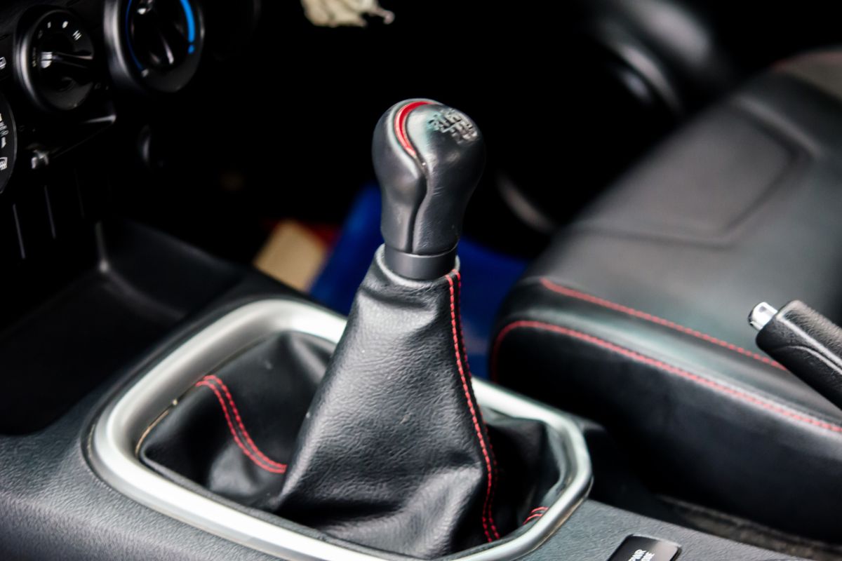 Close-up of a worn car gear shift lever with a red arrow highlighting looseness.